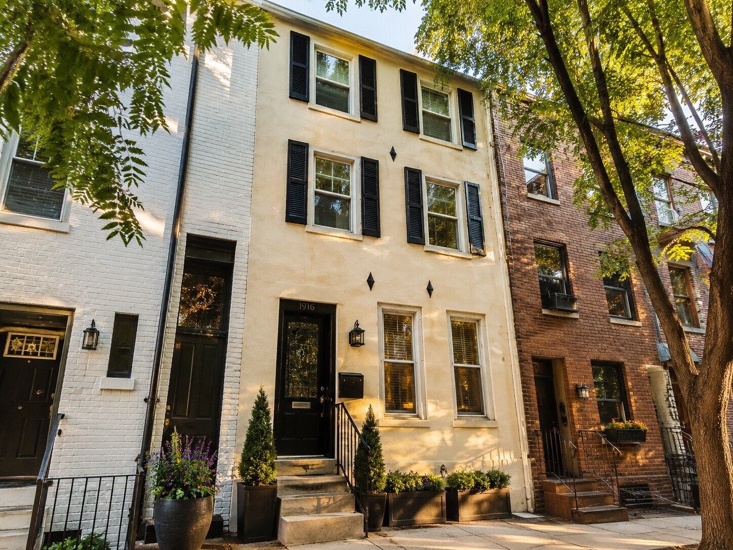 Three-story cream stucco rowhome exterior in Northern Liberties with black shutters and street trees